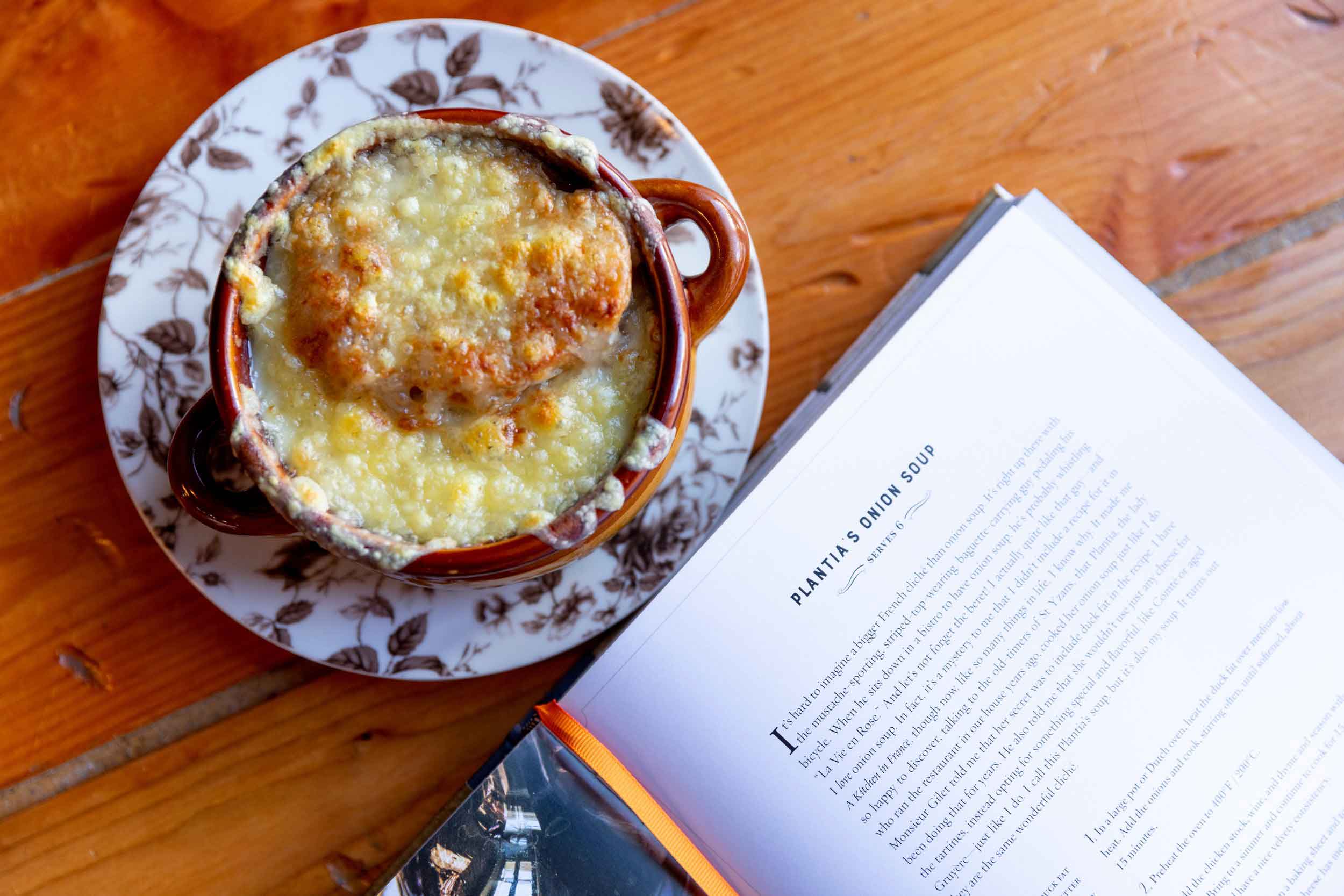 A Bowl Of Soup On A Plate Next To A Book